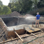 worker spraying water on concrete pool foundation Signature Pools