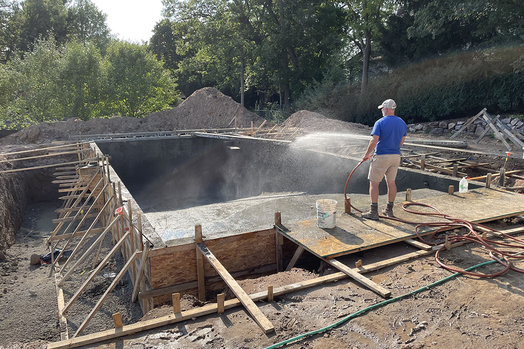 worker spraying water on concrete pool foundation Signature Pools