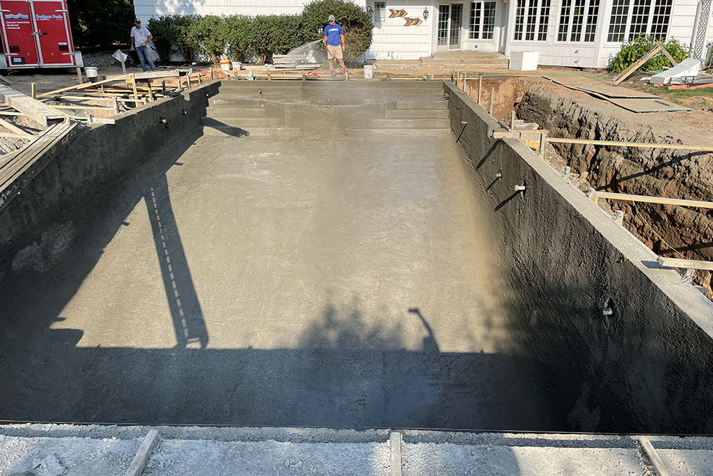 worker spraying water on concrete pool foundation Signature Pools